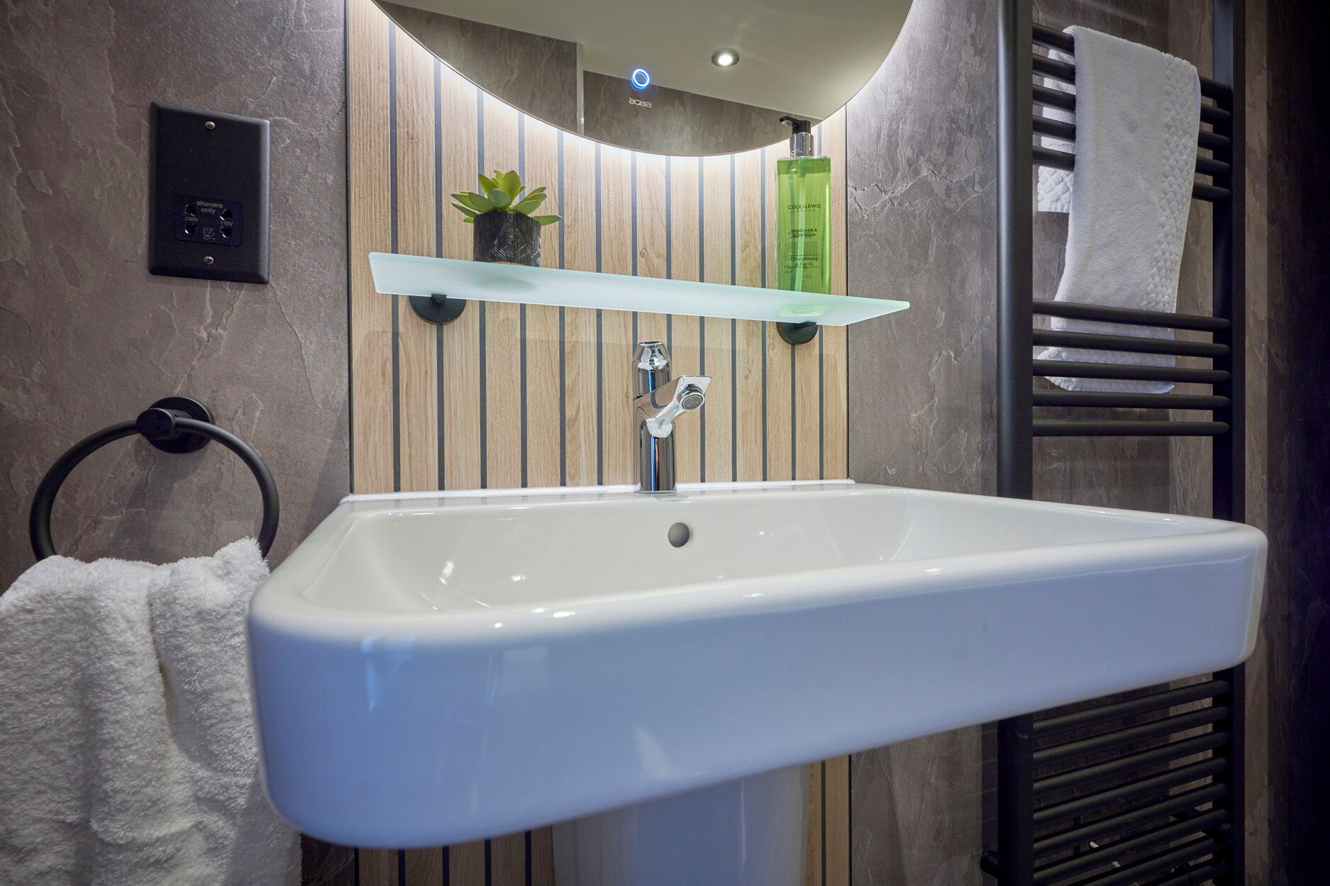 A bathroom with a white sink, a towel rack, a shelf with a plant, and a towel rack with a towel.
