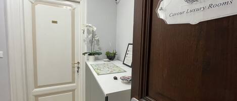 Une chambre d’hôtel avec une porte en bois portant l’inscription « AD Caviar, chambres de luxe », une porte blanche avec une plaque numérotée, une petite table avec une plante et un certificat encadré.