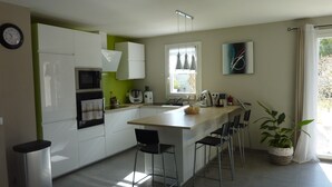Una cocina moderna con armarios blancos, una isla central con taburetes de bar, microondas, hervidor y una ventana con cortinas.