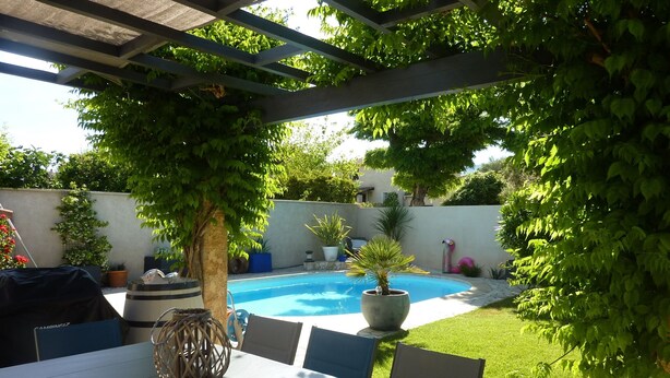 Un patio techado con piscina, mobiliario exterior y abundante vegetación.