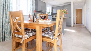 Un comedor con una mesa y sillas de madera, una botella de vino y un cuenco de fruta.