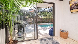Eine Terrasse mit Grill, Pool und einem Korbwäschesessel.