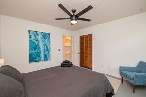 Relax in this serene bedroom with a large bed, ceiling fan, and wall-mounted light fixture.