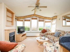 Una sala de estar con chimenea, televisor, sofá floral y ventilador de techo.