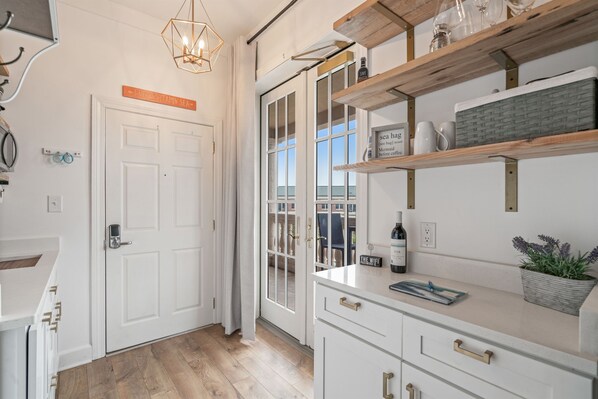 A modern kitchen with white cabinetry, wooden shelves, and a view to the outside.