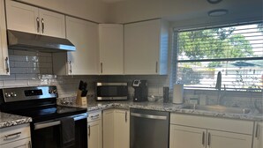Een moderne keuken met witte kasten, roestvrijstalen apparatuur, een magnetron en een raam met jaloezieën.
