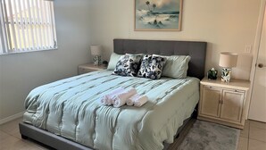 Een keurig opgemaakt slaapkamer met een bed, twee nachtkastjes, een schilderij en een raam met zonwering.