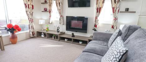 A living room with a grey sofa, a flat-screen TV, and a vase with red flowers.