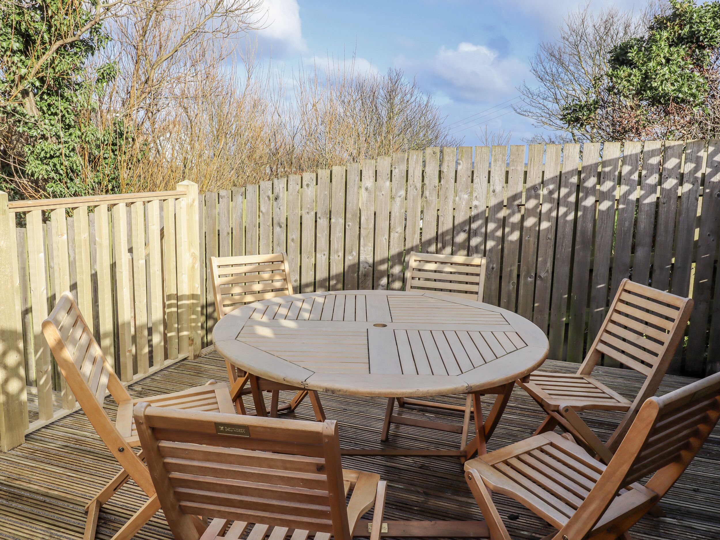 A round wooden table with four chairs, surrounded by a wooden deck and a wooden fence.