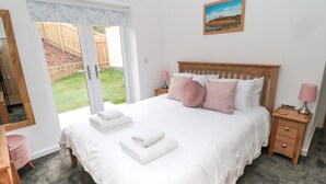 A bedroom with a large bed, a wooden headboard, two bedside tables with lamps, and a view through a sliding glass door to a backyard.