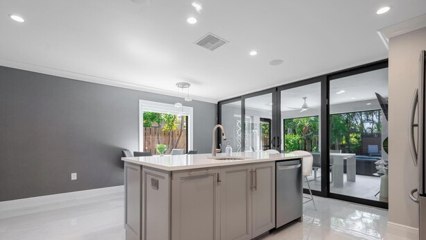 A modern kitchen with a large island, a window, and a view of an outdoor patio. - Stylish & Bright 3-Bedroom Home with Backyard, Bikes & Pool by Esthetic Stays (Naples)