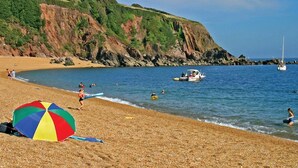 Una playa de piedras, una sombrilla colorida y un velero en el agua.