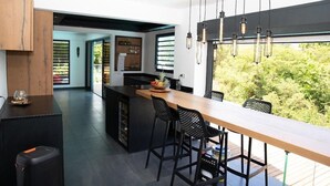 Een moderne keuken met een houten kookeiland, zwarte barkrukken en hangende pendelverlichting.