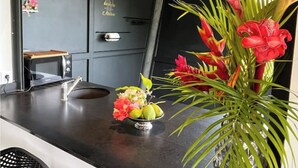 Een moderne keuken met een magnetron, een klein tafeltje en een decoratieve plant met rode bloemen.