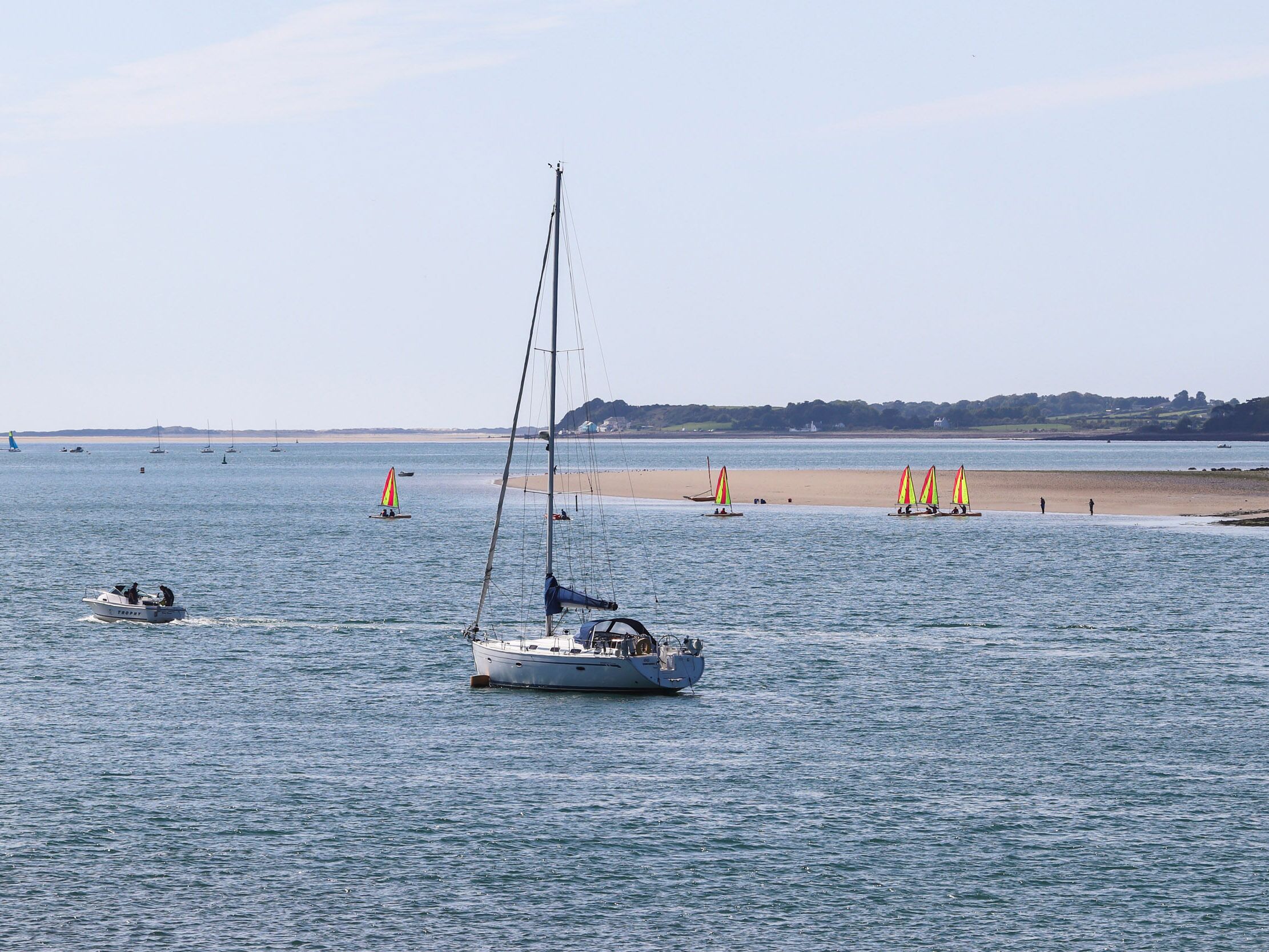 A calm bay with sailboats and a sandy beach.