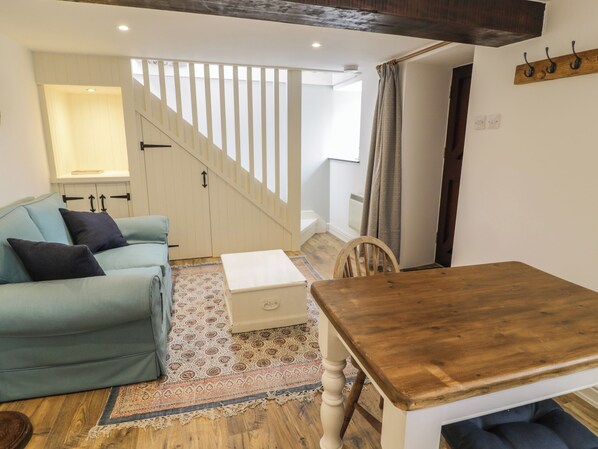 A cozy living room with a sofa, a wooden dining table, and a staircase leading to an upper floor.