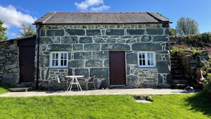 A stone building with two doors and windows, a small outdoor table, and a grassy area in front.