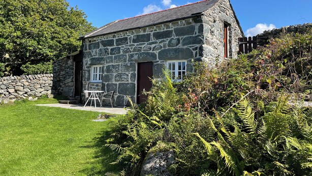 A stone house with a red roof, a stone wall, and a grassy yard.