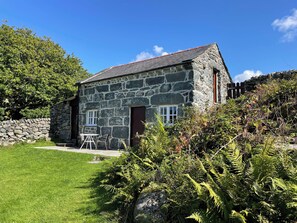 A stone house with a red roof, a stone wall, and a grassy yard.