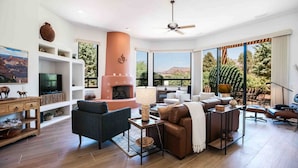 A spacious living room with a fireplace, comfortable seating, a television, and large windows offering a view of the outdoors. - Luxury West Sedona home close to everything (Sedona)