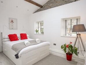 A white bedroom with a bed, red pillows, a bedside lamp, a small window, and a potted plant.