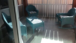 A balcony with wicker furniture, including two chairs and a small table, and a white fence in the background. - Beautiful 2 bedroom 2 Bath directly across from Gulf (North Redington Beach)