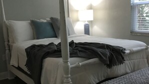 A four-poster bed with a bench at the foot, a bedside table with a lamp, and a window with blinds. - Beautiful 2 bedroom 2 Bath directly across from Gulf (North Redington Beach)