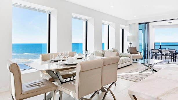 Een moderne, goed verlichte kamer met een grote eettafel, comfortabele zitplaatsen en uitzicht op de oceaan.