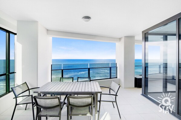 Enjoy ocean views from this spacious balcony with a dining table and chairs, surrounded by glass railings.
