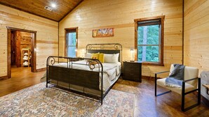 Un dormitorio de cabaña de madera con una cama de metal, una silla y un cuadro en la pared.