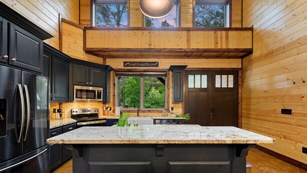 Una cocina moderna con una isla grande, armarios oscuros, electrodomésticos de acero inoxidable y vistas al exterior.