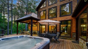 Una cabaña de madera con hidromasaje, mobiliario exterior y un porche cubierto.