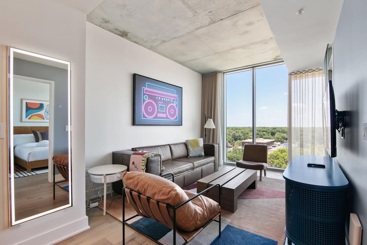 A modern living room with a sofa, coffee table, and a large window offering a city view.