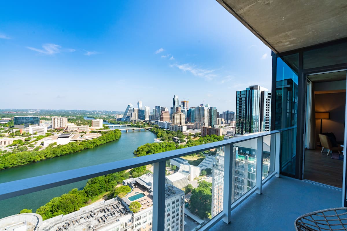 A high-rise building with a balcony overlooking a cityscape, river, and greenery.
