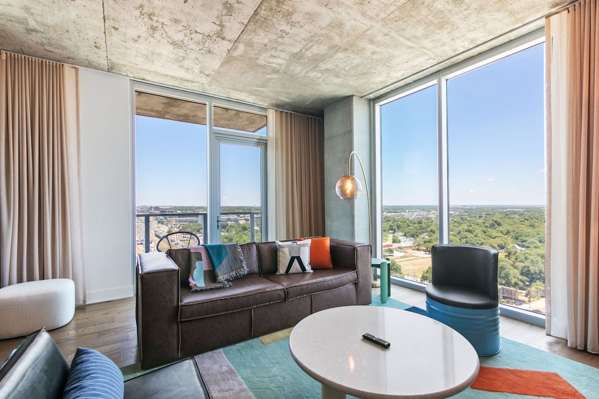 A modern living room with a brown leather sofa, a round coffee table, and a view of a cityscape through large windows.