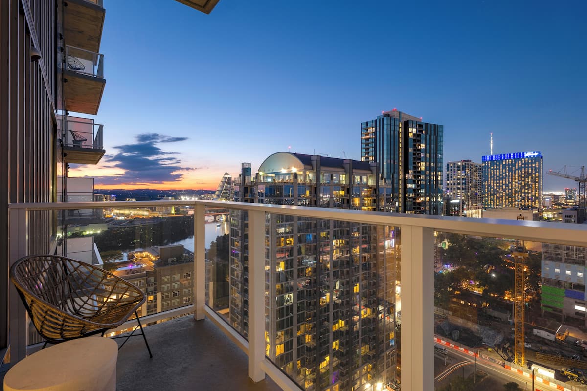 A balcony with a view of a cityscape at dusk, featuring high-rise buildings and a river.