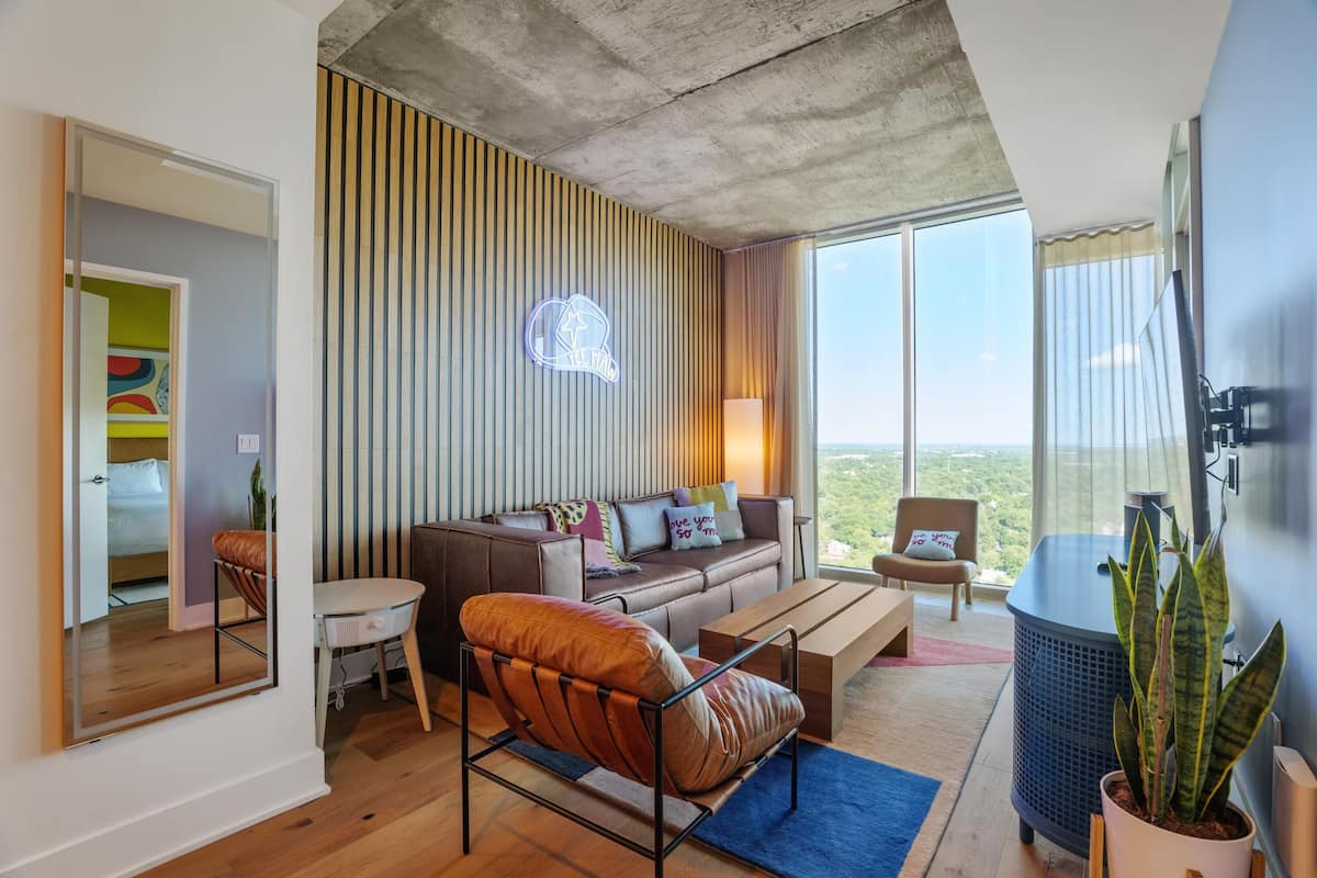 A modern living room with a sofa, armchair, and coffee table. There is a large window with a view of the outdoors.