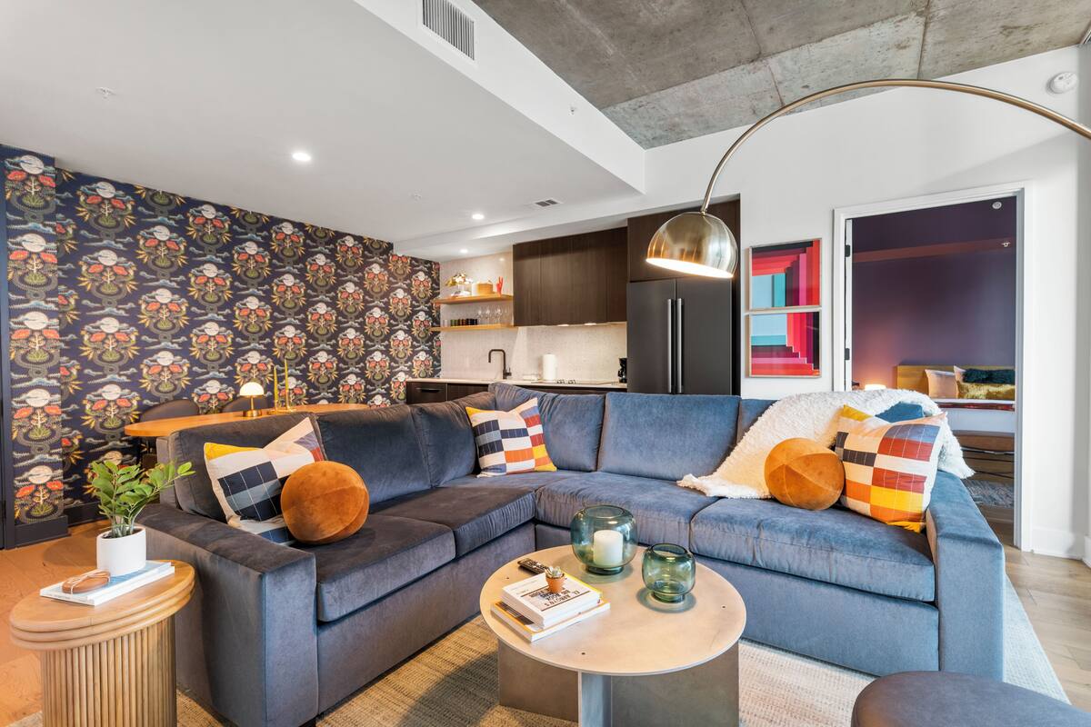 A modern living room with a sectional sofa, a round coffee table, and a kitchen area in the background.