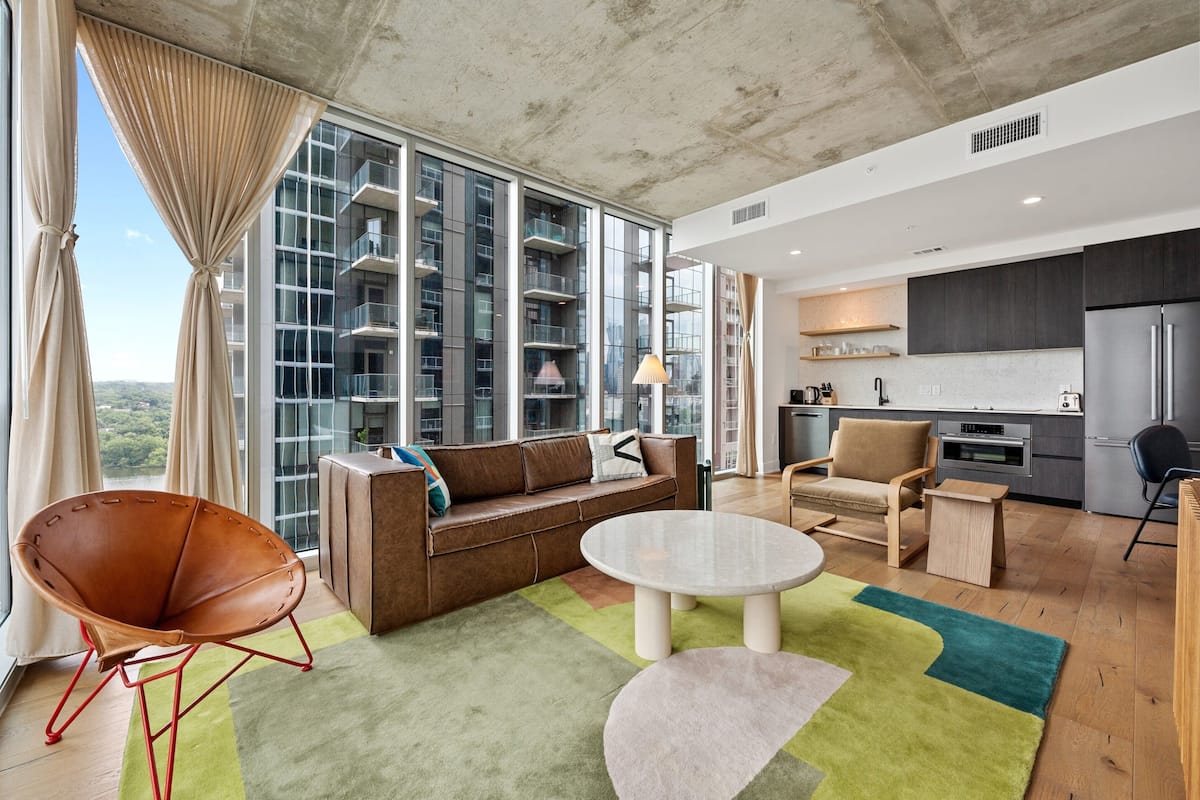 A modern living room with a sofa, a chair, a table, and a view of a high-rise building.
