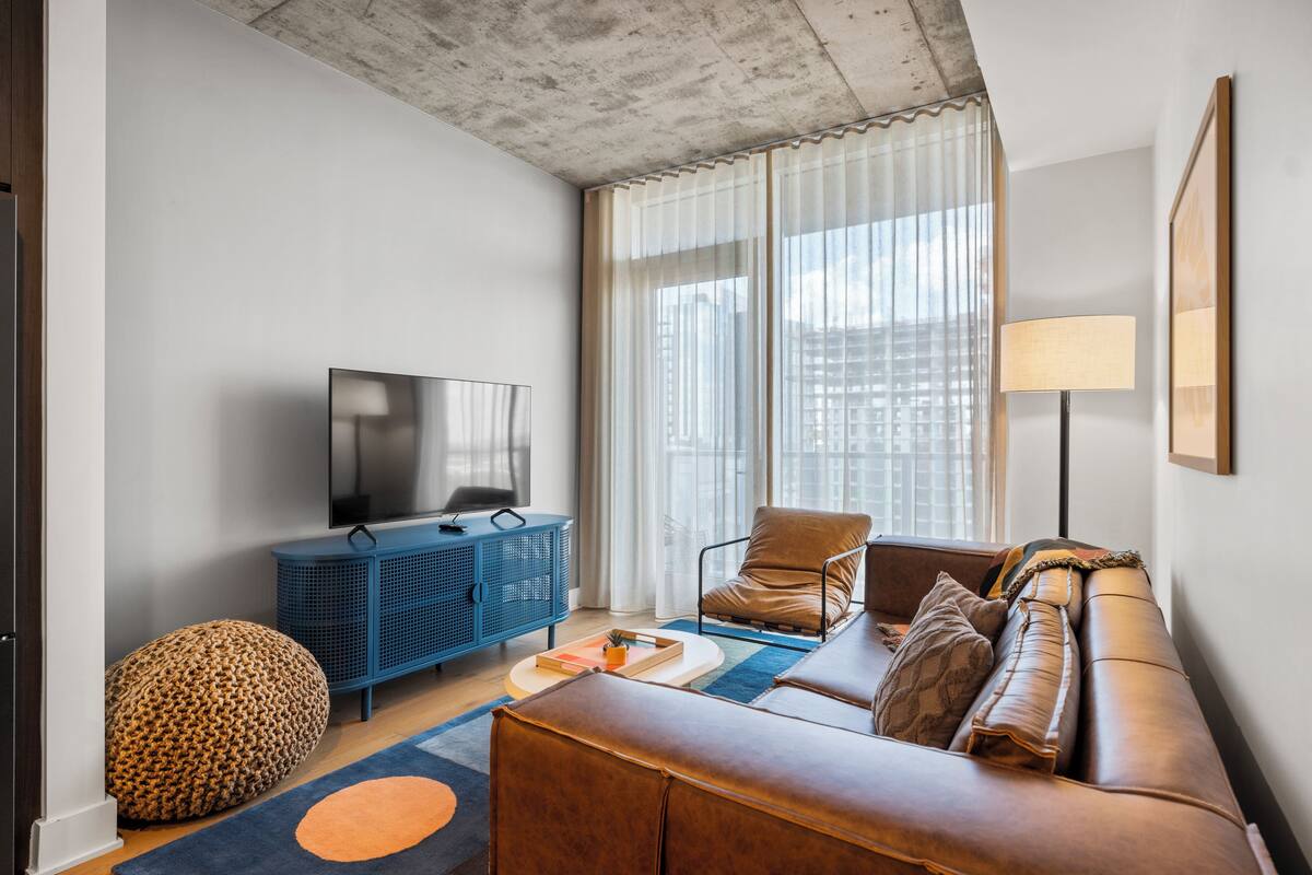 A modern living room with a sofa, a blue cabinet, a television, and a large window with curtains.