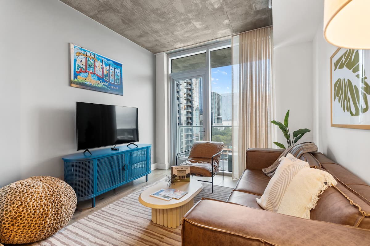 A modern living room with a flat-screen TV, a blue cabinet, a brown sofa, and a large window with a city view.