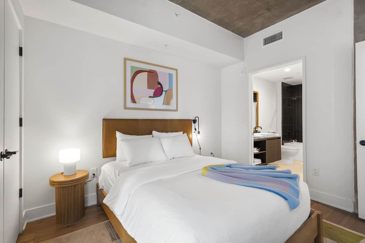 A neatly made bed with white linens, a bedside lamp, and a colorful blanket.