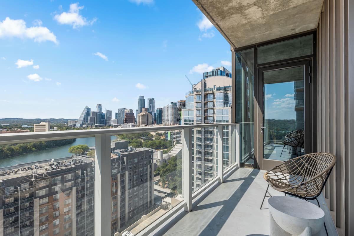 A balcony with a view of a city skyline, a glass door, and a wicker chair.