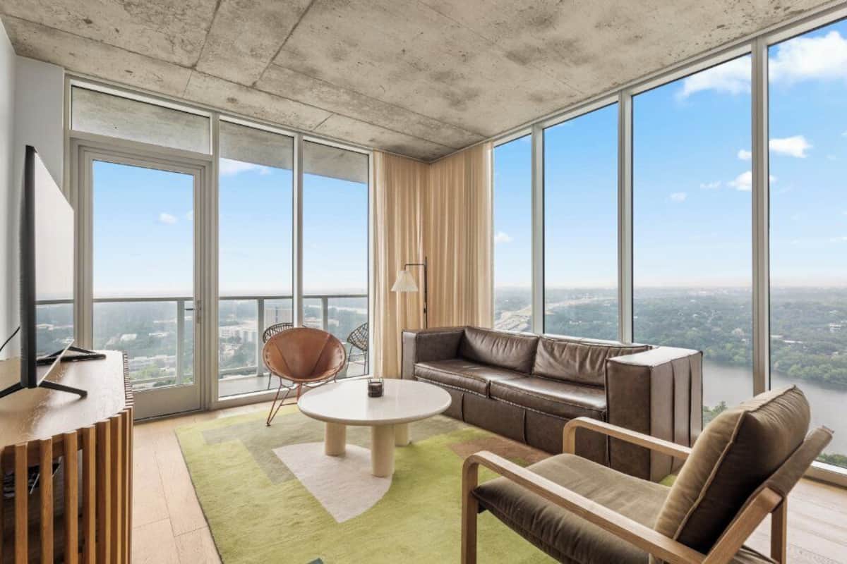 A high-rise apartment with a large balcony, a leather sofa, a round coffee table, and a TV on a wooden stand.