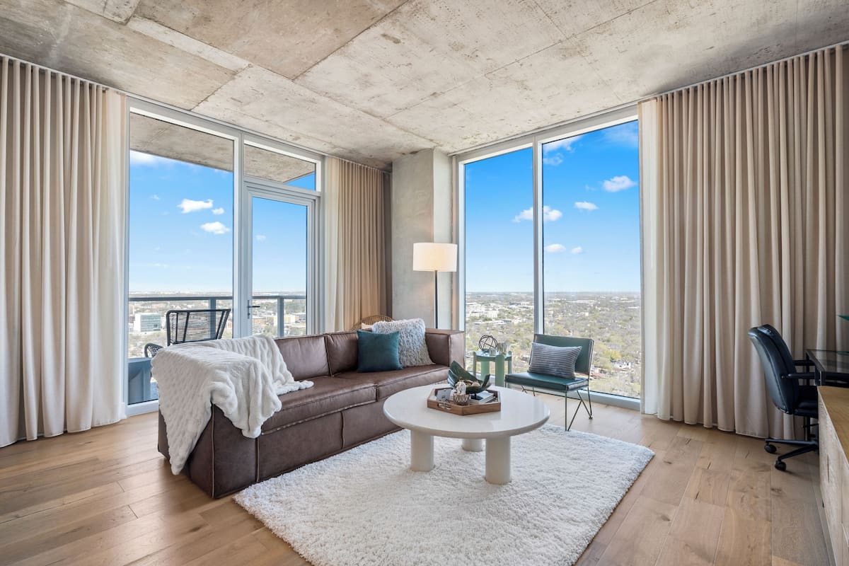 A modern living room with a brown leather sofa, a round coffee table, and a view of the city through large windows.