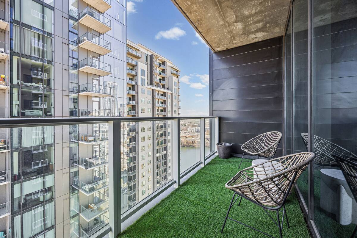 A balcony with artificial grass, wicker chairs, and a view of high-rise buildings.