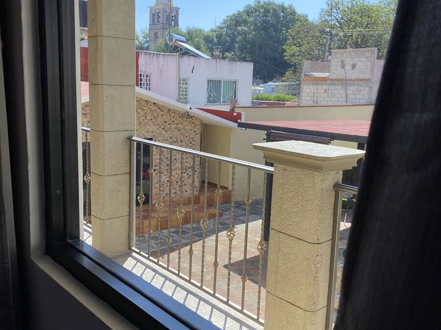A balcony with a view of a building with a clock tower, a red roof, and a clear blue sky.
