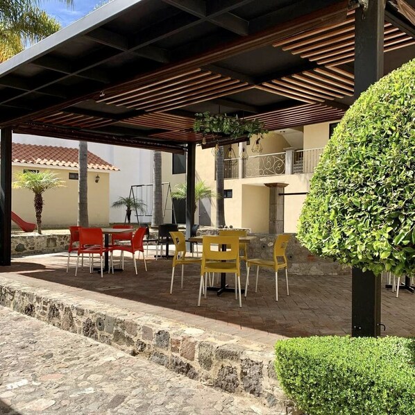 An outdoor patio with tables and chairs, a stone wall, and a well-maintained hedge.