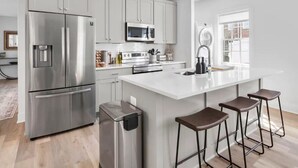 A modern kitchen with stainless steel appliances, a central island with stools, and a large window providing natural light. - ★1/2 Block to King Street, King Bed ~ Free Parking★ (Alexandria)
