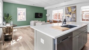 A modern kitchen with a central island, a dining area with a wooden chair, and a living space with a sofa and a TV. - ★1/2 Block to King Street, King Bed ~ Free Parking★ (Alexandria)